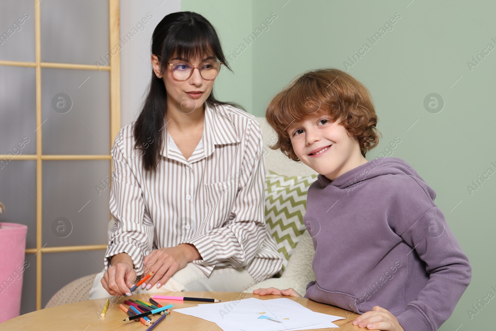 Photo of Boy drawing at table during consultation with psychologist indoors