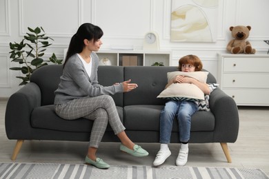 Photo of Scared little boy having therapy session with psychologist in office