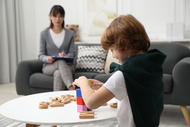 Boy playing with wooden cubes at table while psychologist taking notes, selective focus