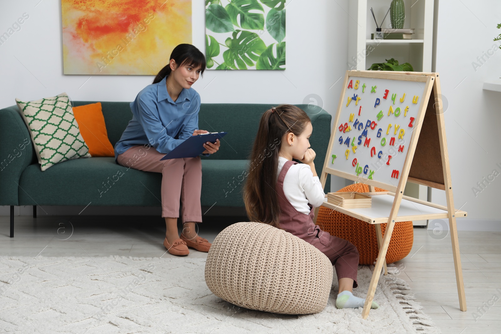 Photo of Girl assembling letters on magnetic board while psychologist taking notes indoors