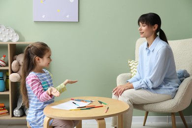 Psychologist having consultation with little girl indoors