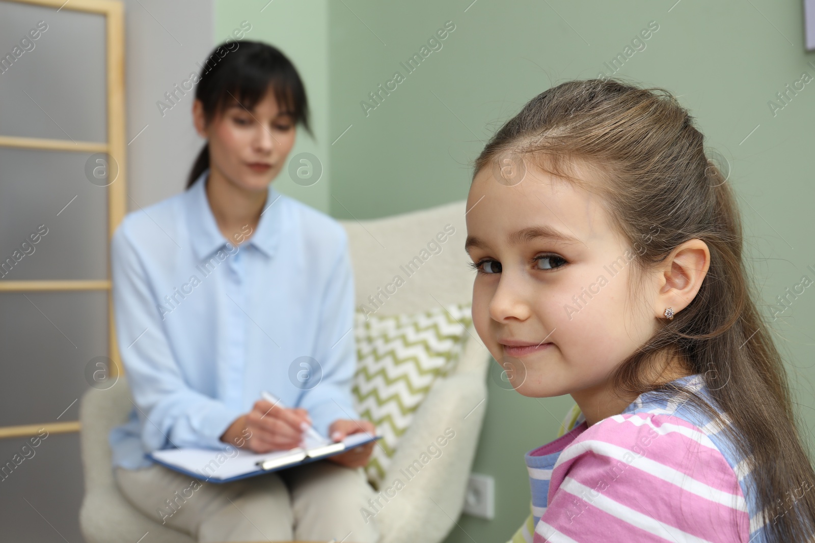 Photo of Little girl having therapy session with psychologist in office, selective focus