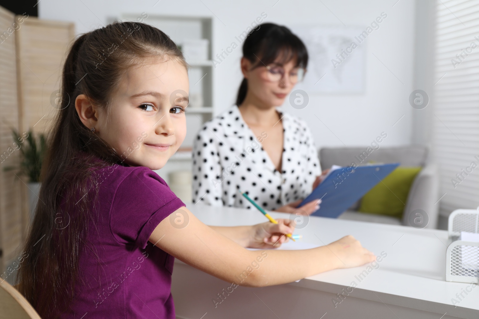 Photo of Little girl drawing at desk while psychologist taking notes, selective focus