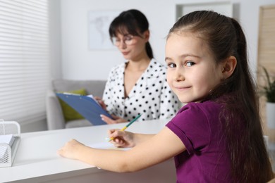 Little girl drawing at desk while psychologist taking notes, selective focus