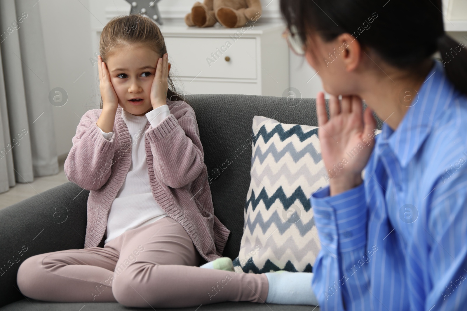 Photo of Psychologist having therapy session with little girl on sofa in office