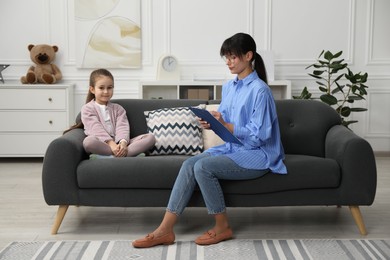 Photo of Psychologist having therapy session with little girl on sofa in office