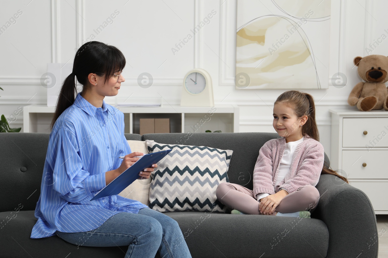 Photo of Psychologist having therapy session with little girl on sofa in office