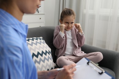 Photo of Psychologist having therapy session with little girl on sofa in office