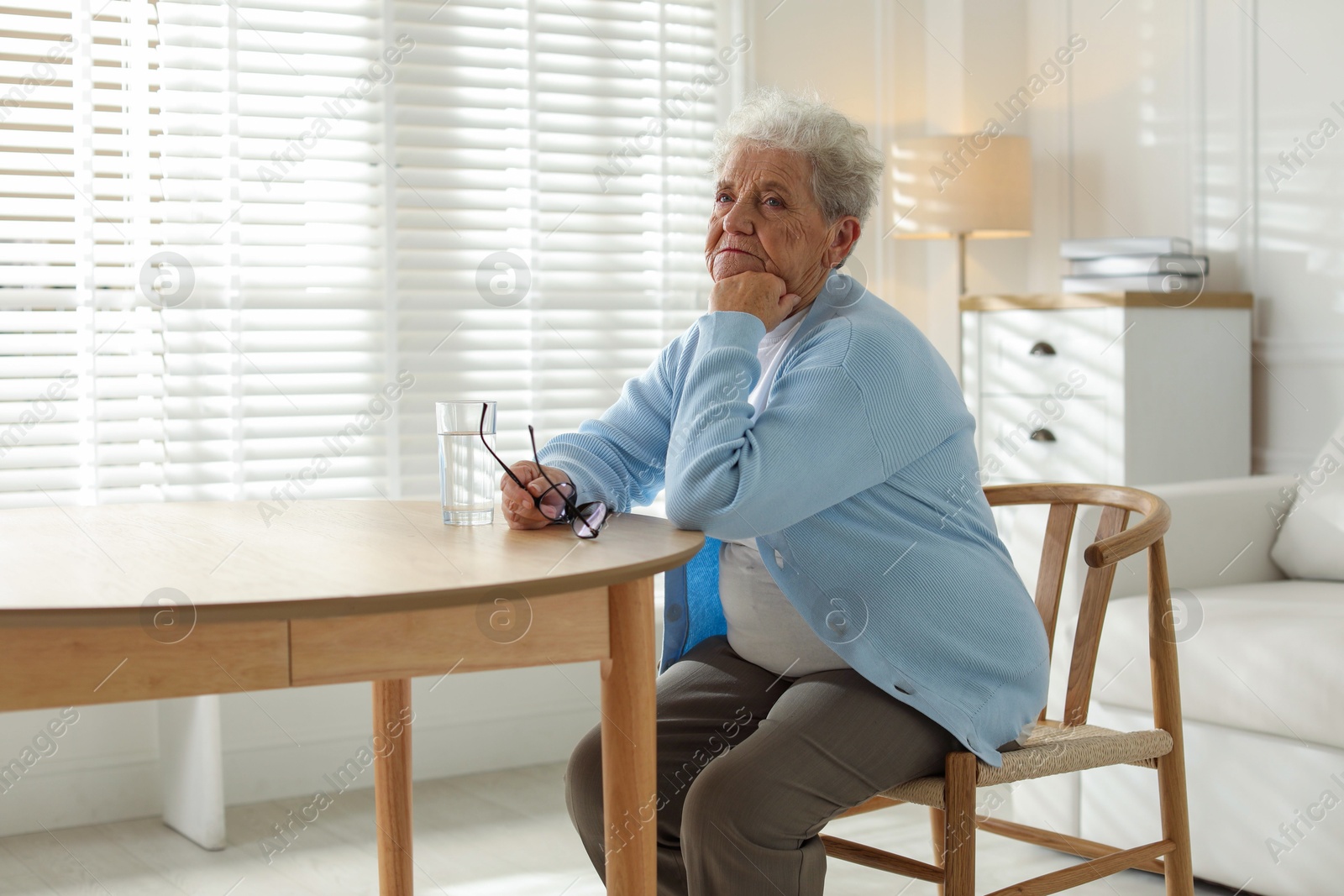 Photo of Thoughtful senior woman feeling lonely at table with glass of water indoors