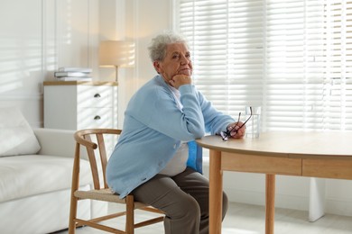 Photo of Thoughtful senior woman feeling lonely at table with glass of water indoors