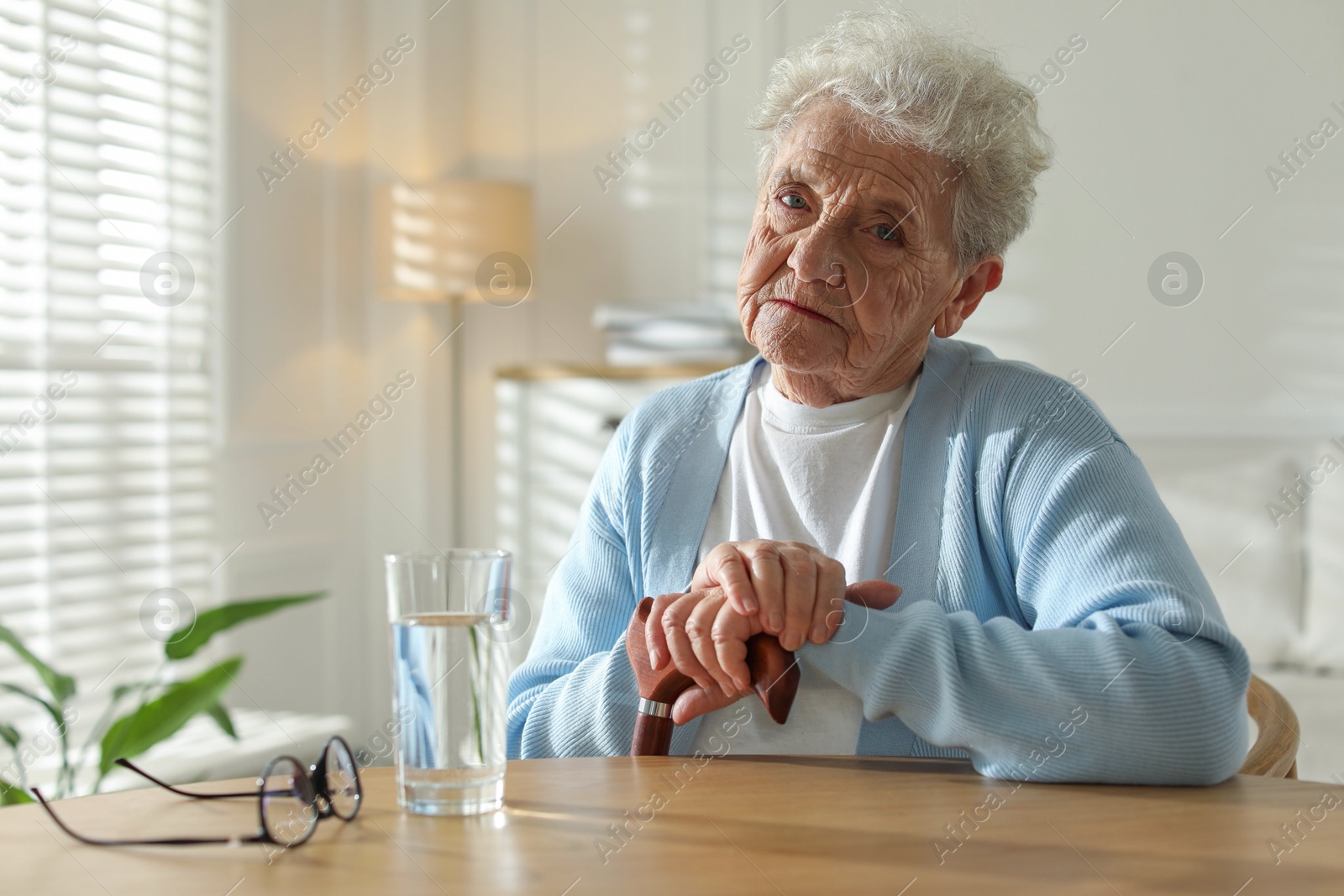 Photo of Thoughtful senior woman feeling lonely at table with glass of water indoors