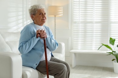 Photo of Lonely senior woman with walking cane sitting on sofa indoors. Space for text