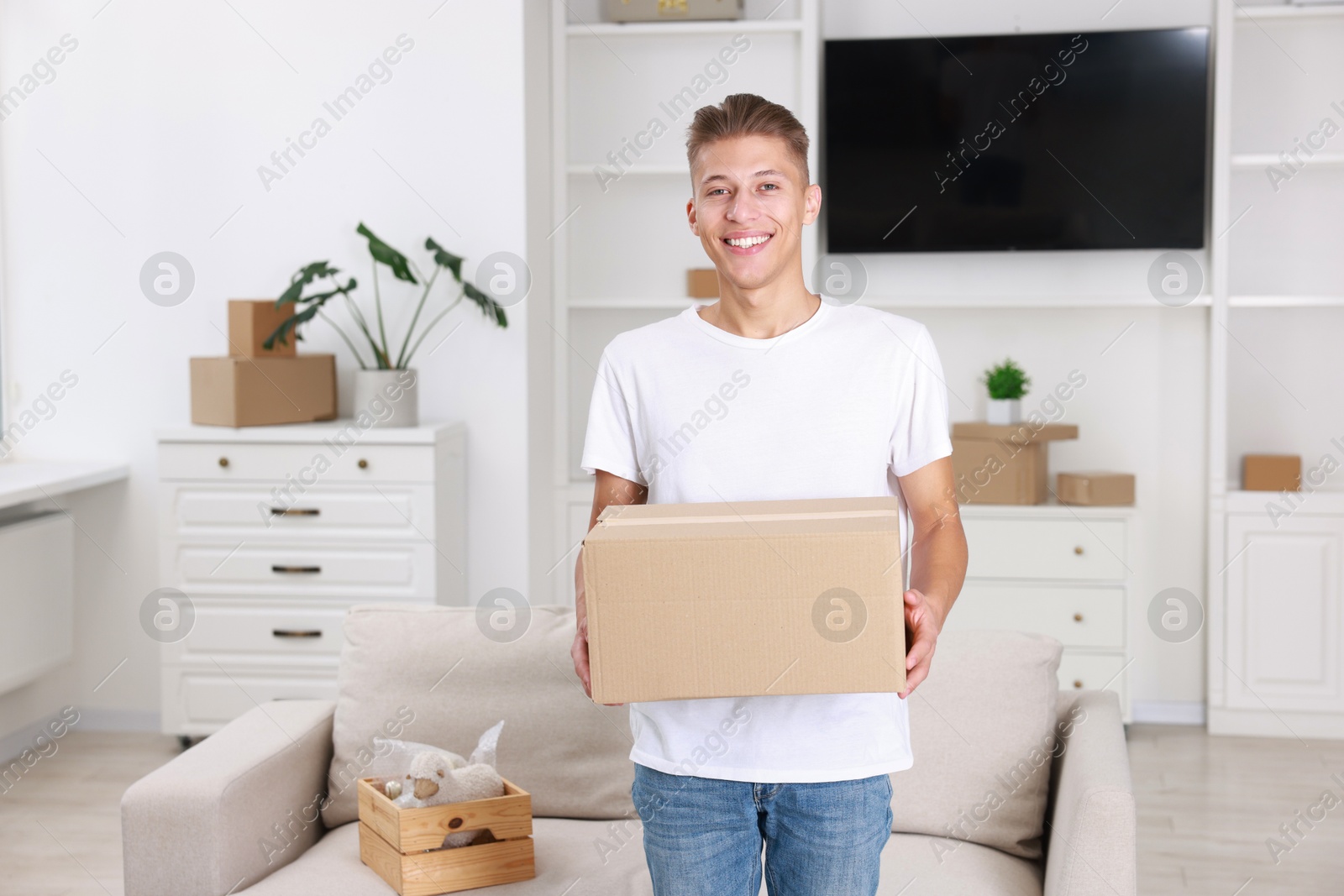 Photo of Happy man with moving box in new apartment. Housewarming party