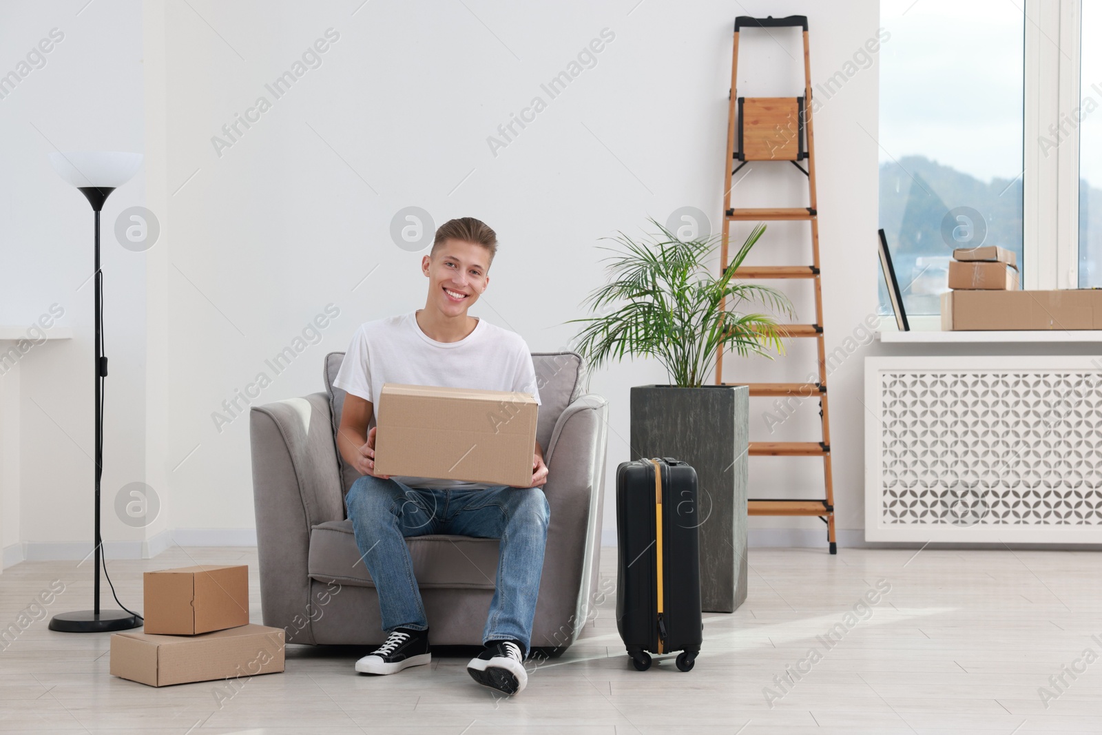 Photo of Happy man with moving boxes and suitcase in new apartment. Housewarming party