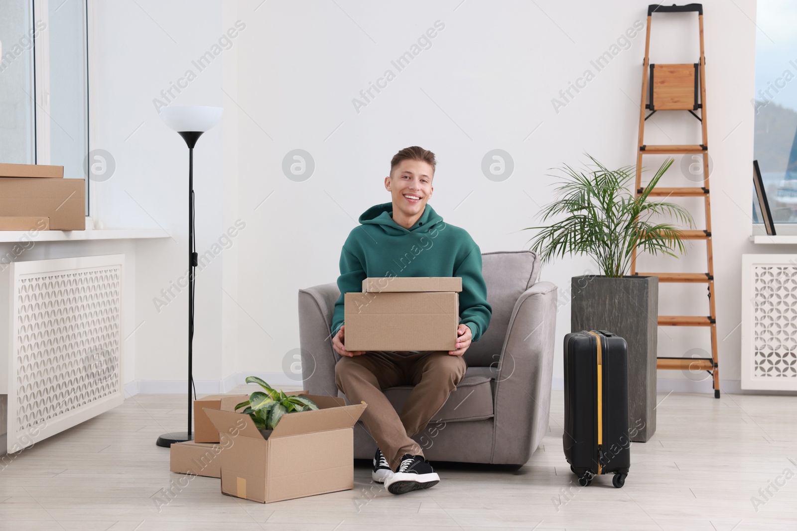 Photo of Happy man with moving boxes and suitcase in new apartment. Housewarming party