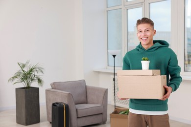 Photo of Happy man with moving boxes and houseplant in new apartment. Housewarming party