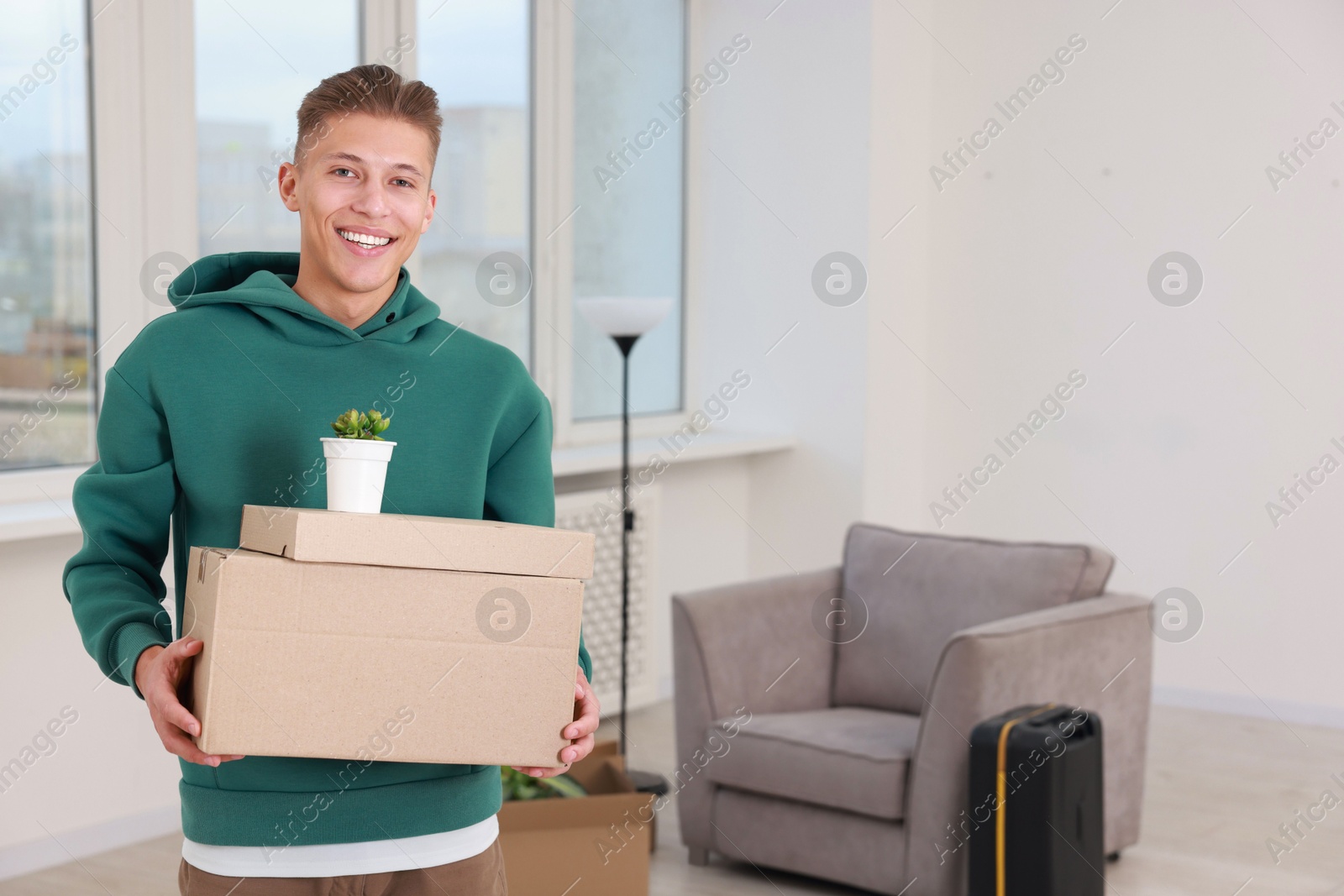 Photo of Happy man with moving boxes and houseplant in new apartment. Housewarming party