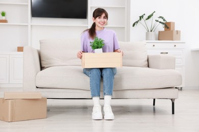 Photo of Happy woman holding wooden crate with stuff on sofa in new apartment. Housewarming party