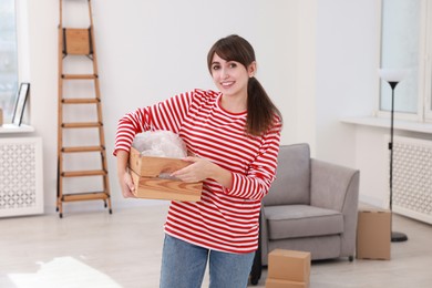 Photo of Happy woman holding wooden crate with stuff in new apartment. Housewarming party