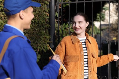 Photo of Woman receiving parcel from postman outdoors. Mail service