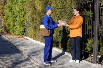 Photo of Woman receiving parcel from postman outdoors. Mail service