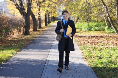 Photo of Happy postman with bag and envelopes outdoors