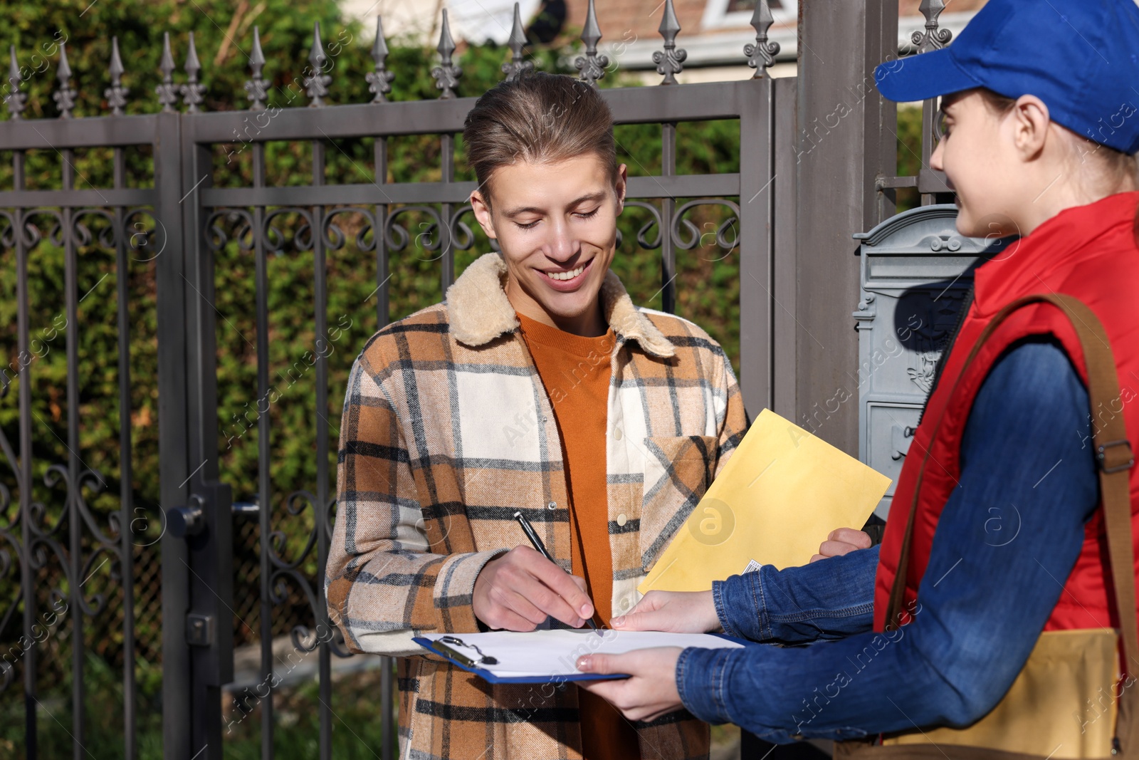 Photo of Man signing papers while receiving parcel from postwoman outdoors