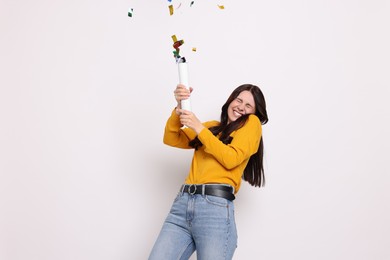 Happy woman blowing up confetti popper on white background. Surprise party