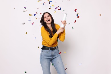 Happy woman blowing up confetti popper on white background. Surprise party