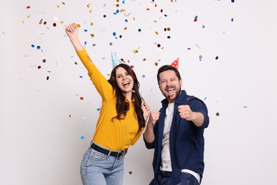 Happy friends in conical paper hats having fun under falling confetti on white background. Surprise party