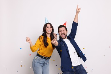 Photo of Happy friends in conical paper hats and flying confetti on white background. Surprise party