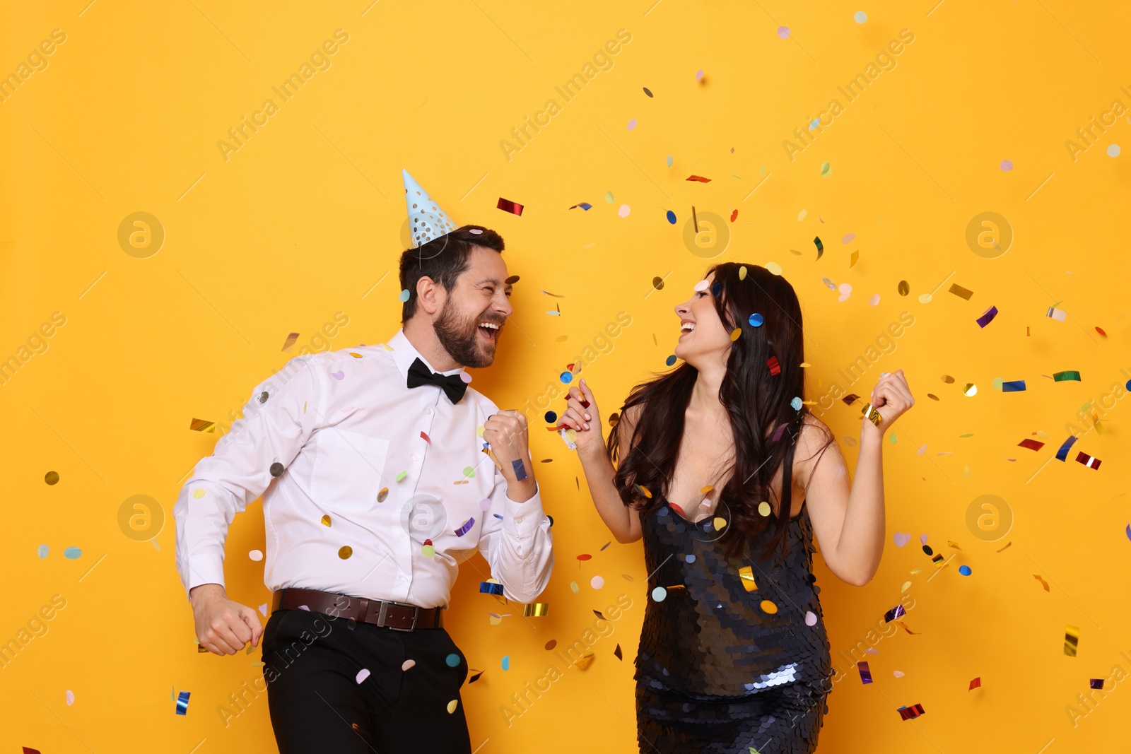 Photo of Happy friends having fun under flying confetti on orange background. Surprise party