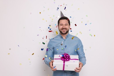 Photo of Happy man with gift box under falling confetti on white background. Surprise party