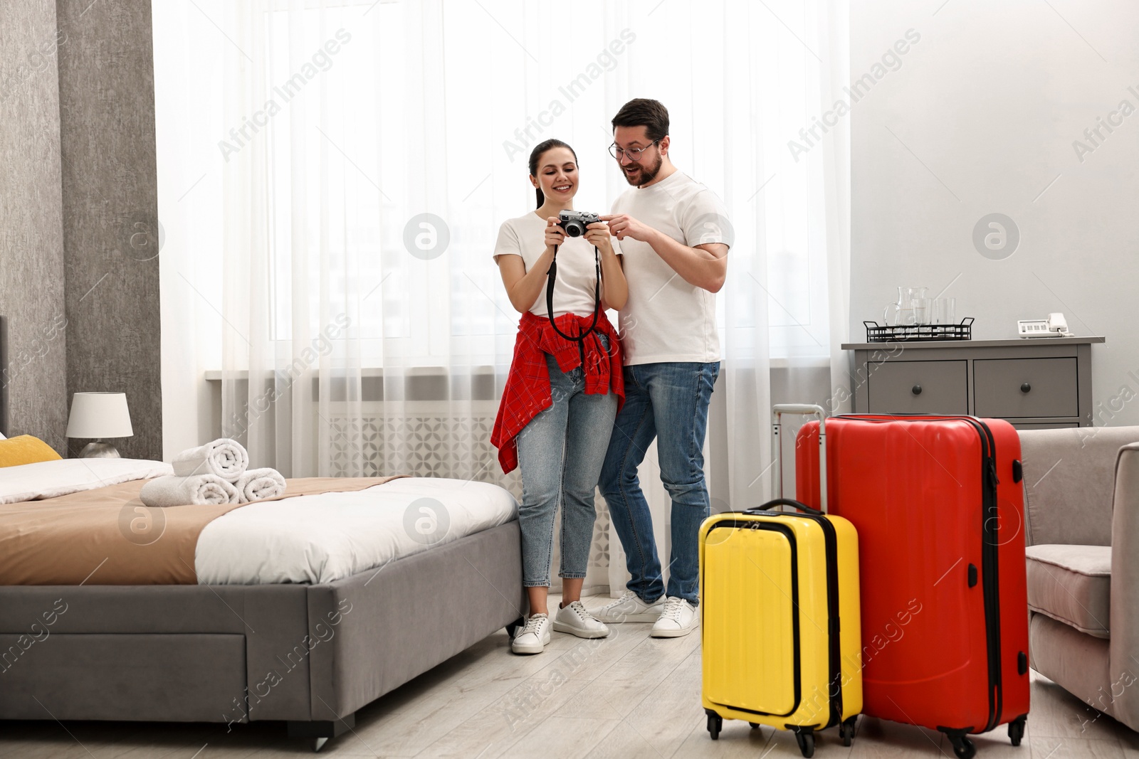 Photo of Happy travellers with camera and suitcases in hotel room