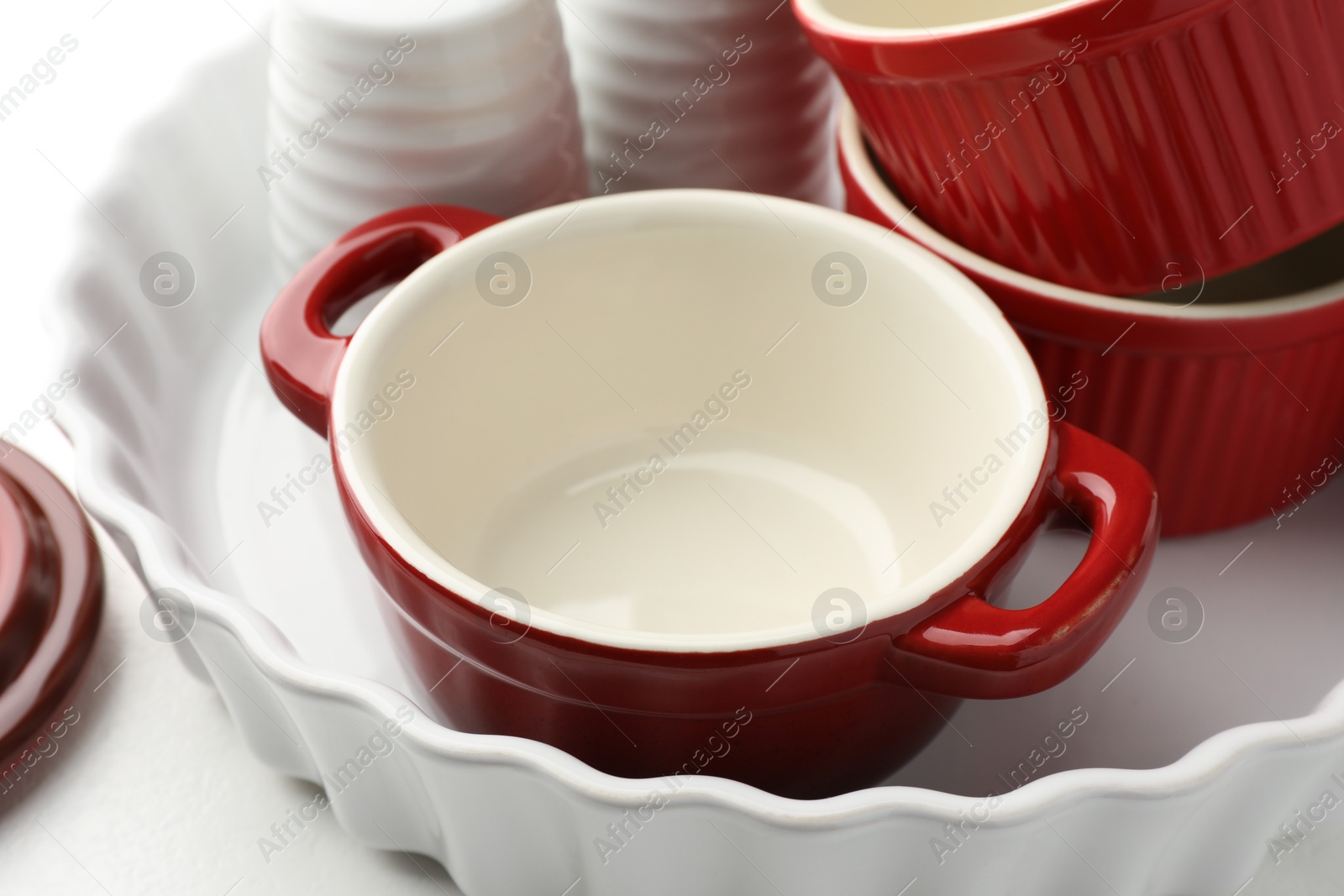 Photo of Different ceramic casseroles and shakers on white table, closeup