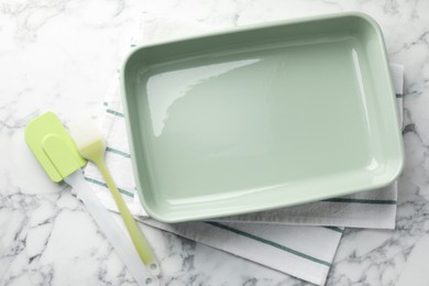 Photo of Ceramic casserole, spatula and brush on white marble table, flat lay