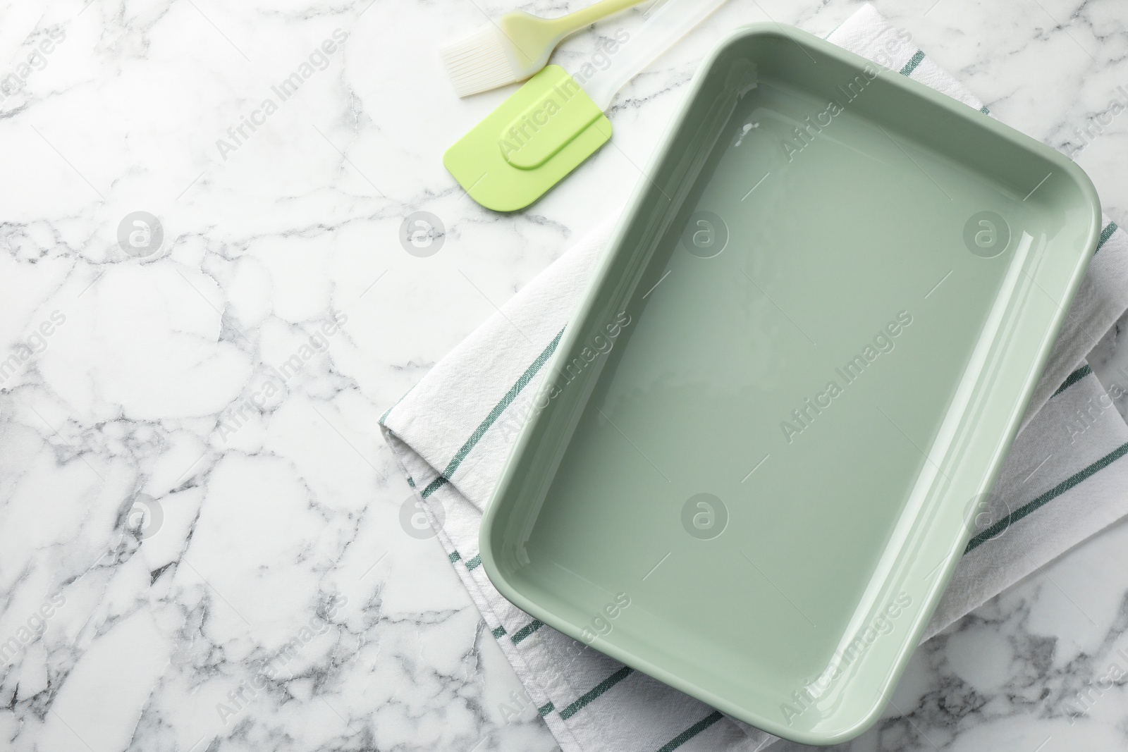 Photo of Ceramic casserole, spatula and brush on white marble table, flat lay. Space for text