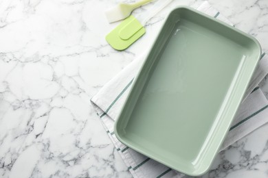 Photo of Ceramic casserole, spatula and brush on white marble table, flat lay. Space for text