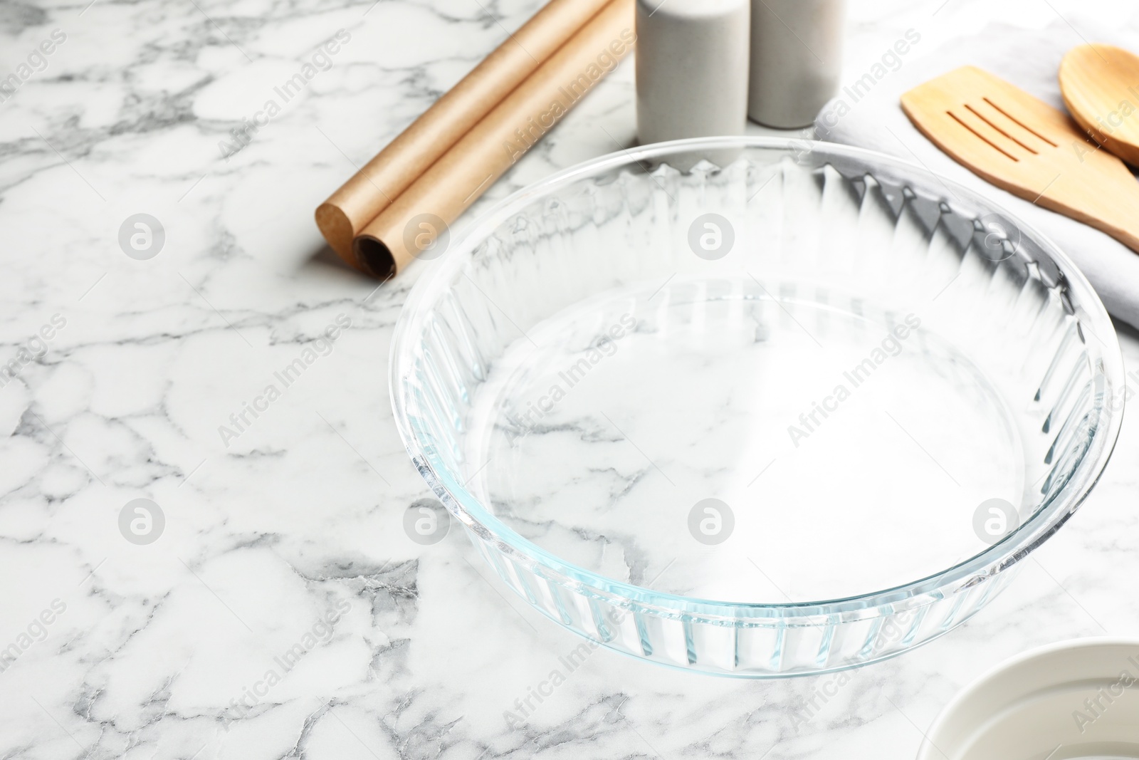 Photo of Glass casserole and other cooking utensils on white marble table, closeup