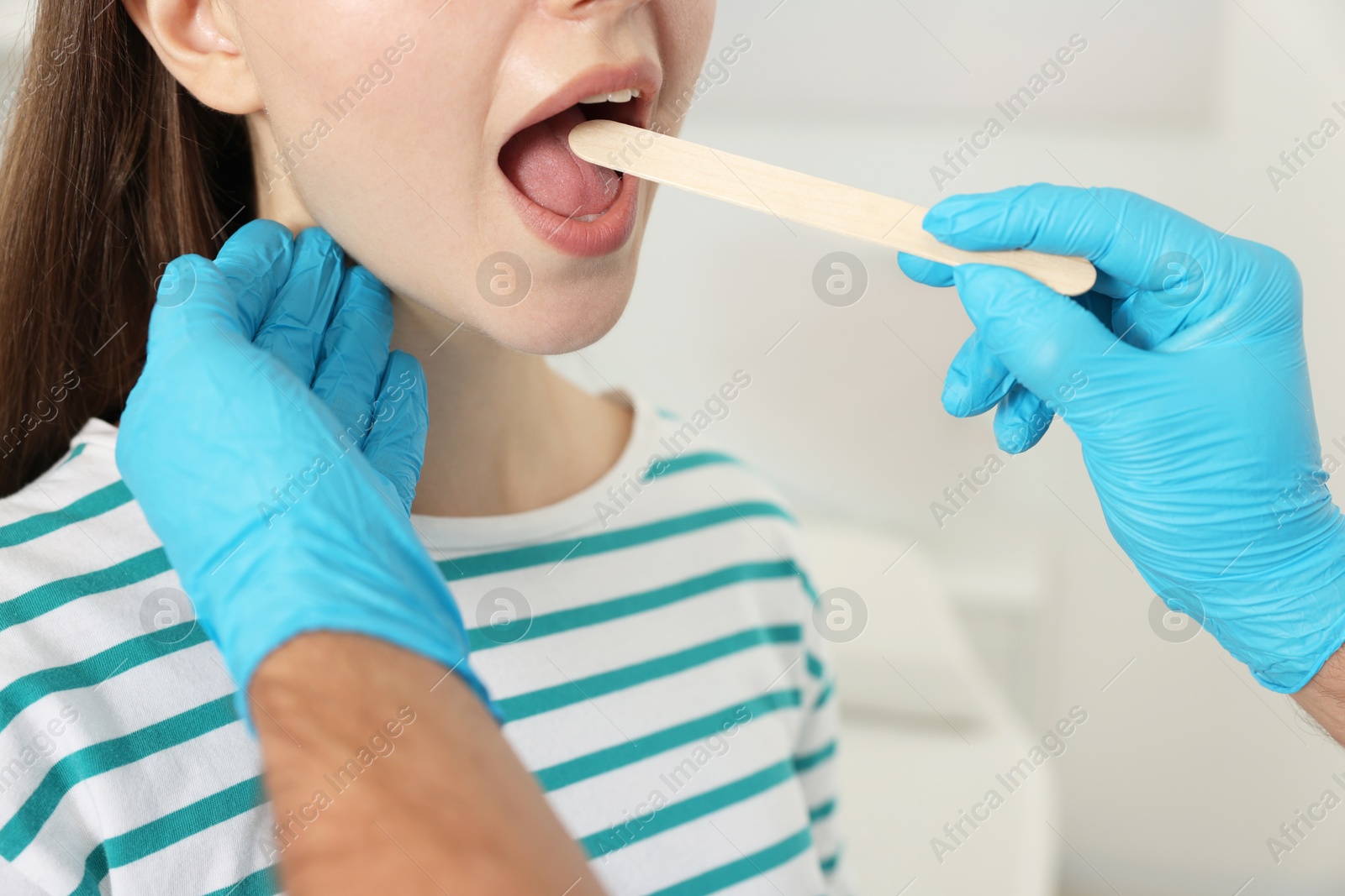 Photo of Doctor examining woman's throat with tongue depressor in clinic, closeup