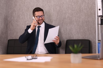 Photo of Banker with document talking on smartphone in office