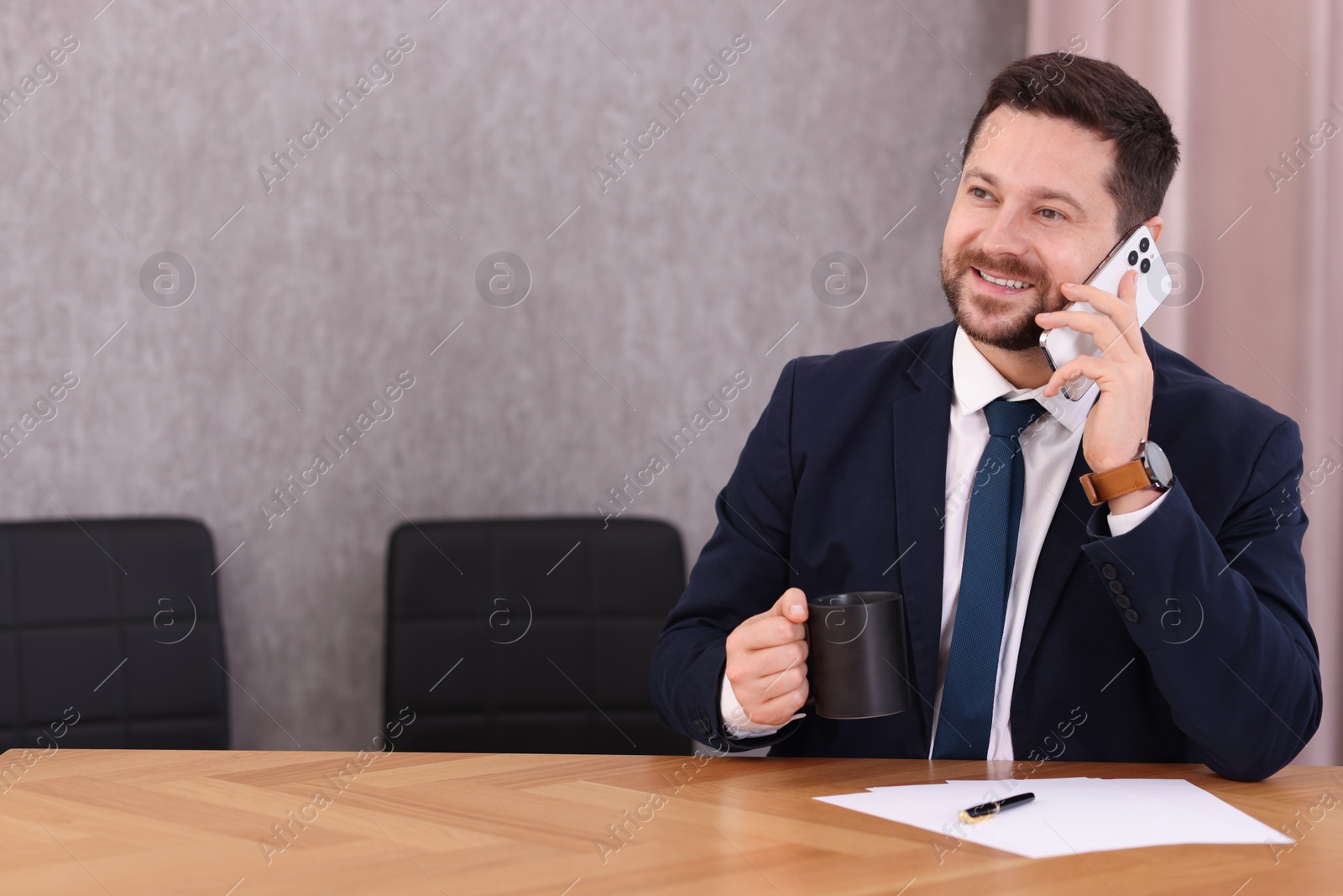 Photo of Banker with cup of drink talking on smartphone at wooden table in office. Space for text