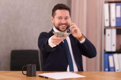 Photo of Banker with dollar banknotes talking on smartphone at table in office, selective focus