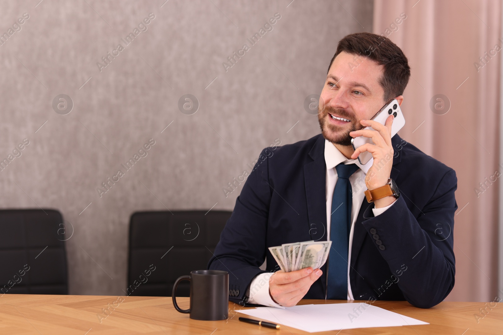 Photo of Banker with dollar banknotes talking on smartphone at table in office. Space for text