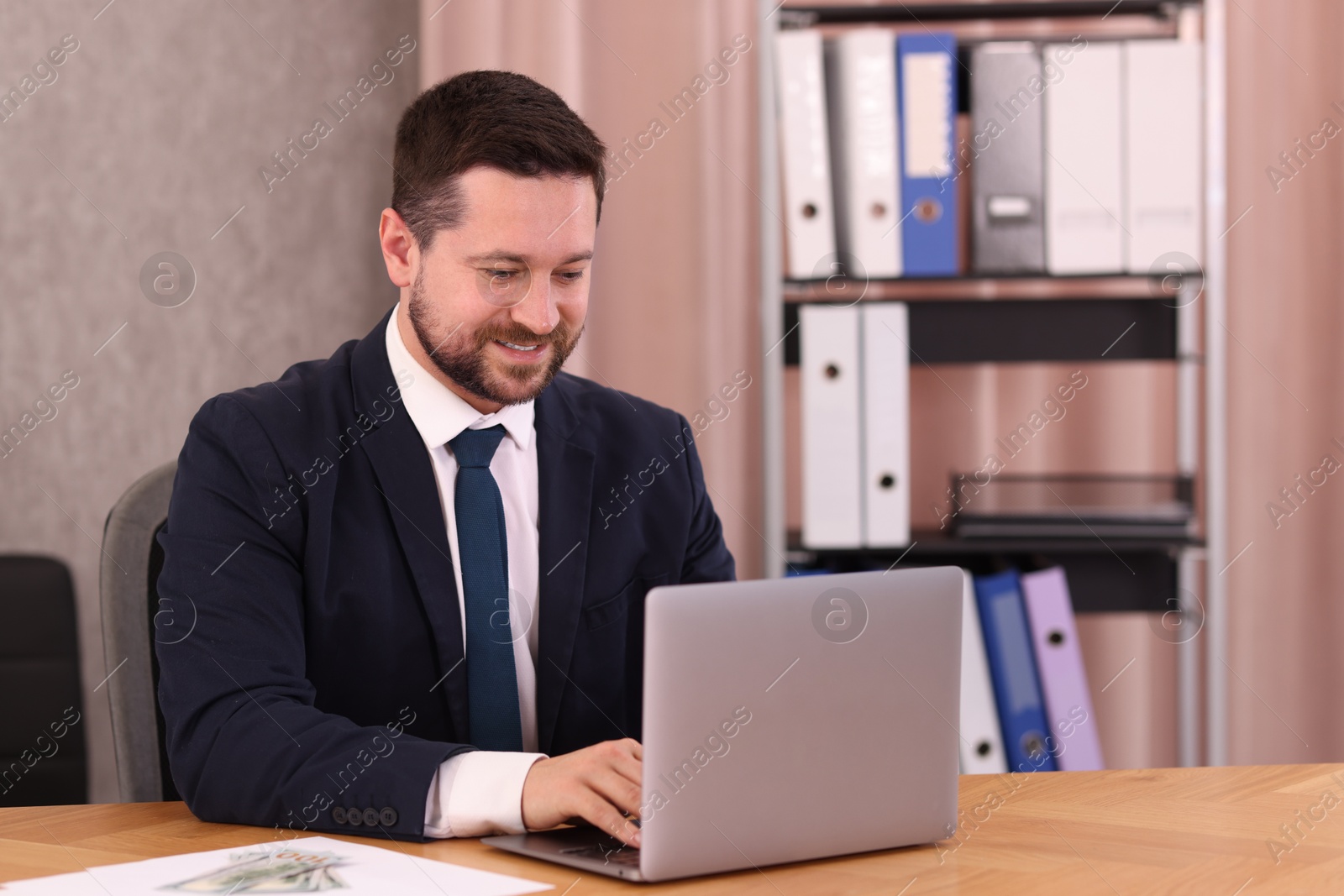 Photo of Banker working with laptop at wooden table in office