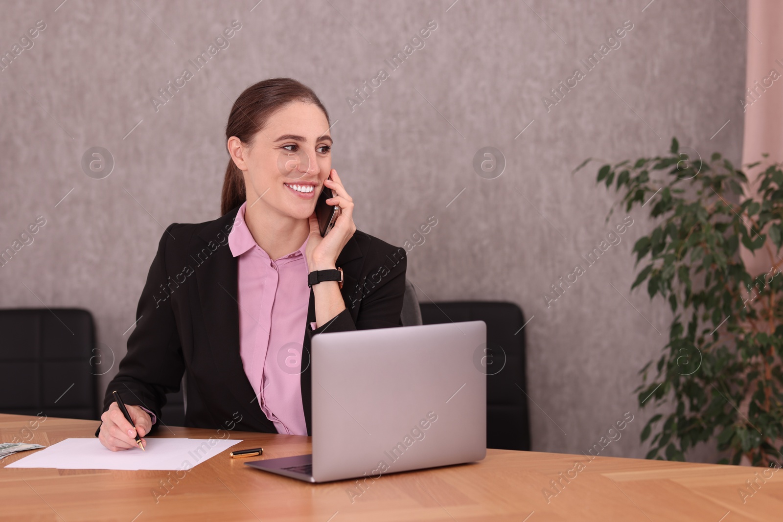 Photo of Banker talking on smartphone while working with documents at table in office