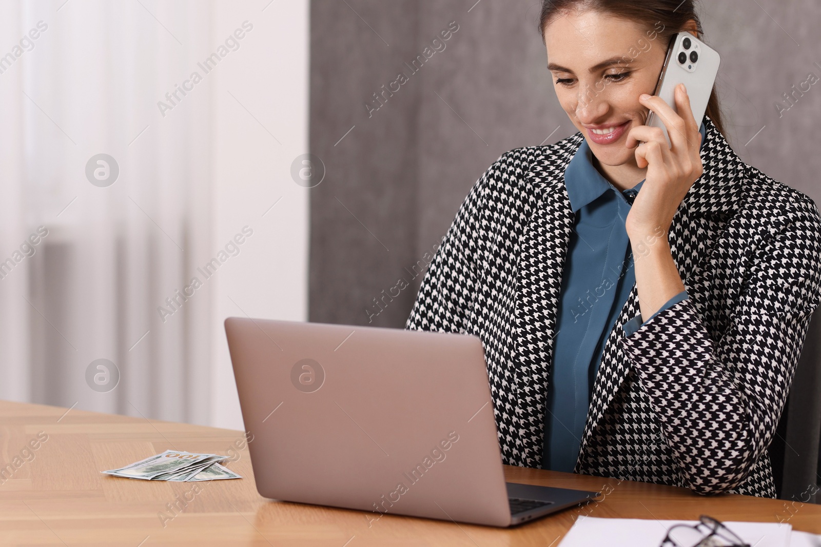 Photo of Banker talking on smartphone while working with laptop at table in office