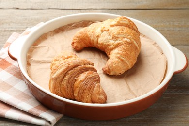 Photo of Ceramic casserole with croissants and baking parchment paper on wooden table, closeup