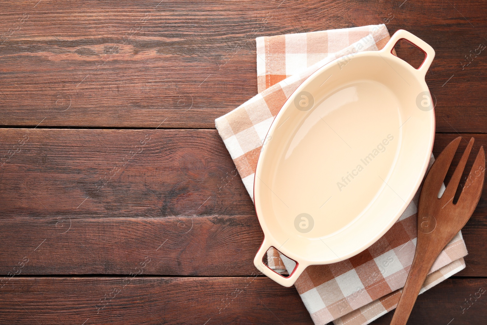 Photo of Ceramic casserole and slotted turner on wooden table, top view. Space for text