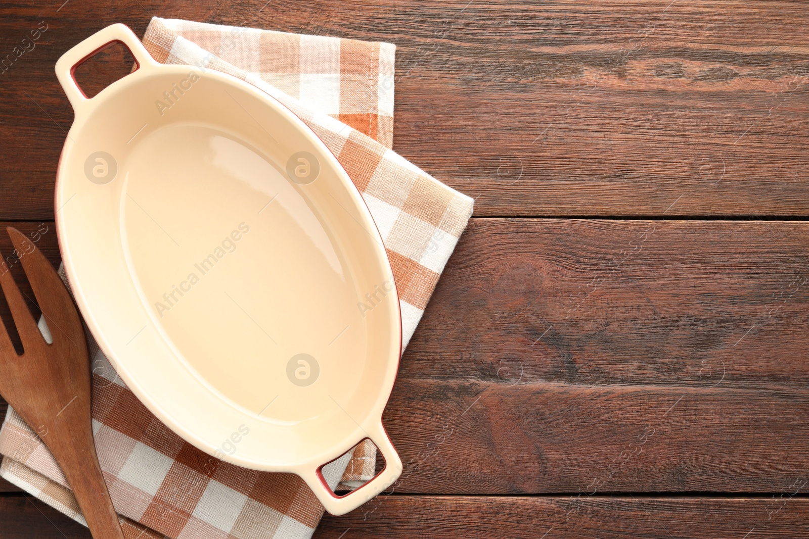 Photo of Ceramic casserole and slotted turner on wooden table, top view. Space for text